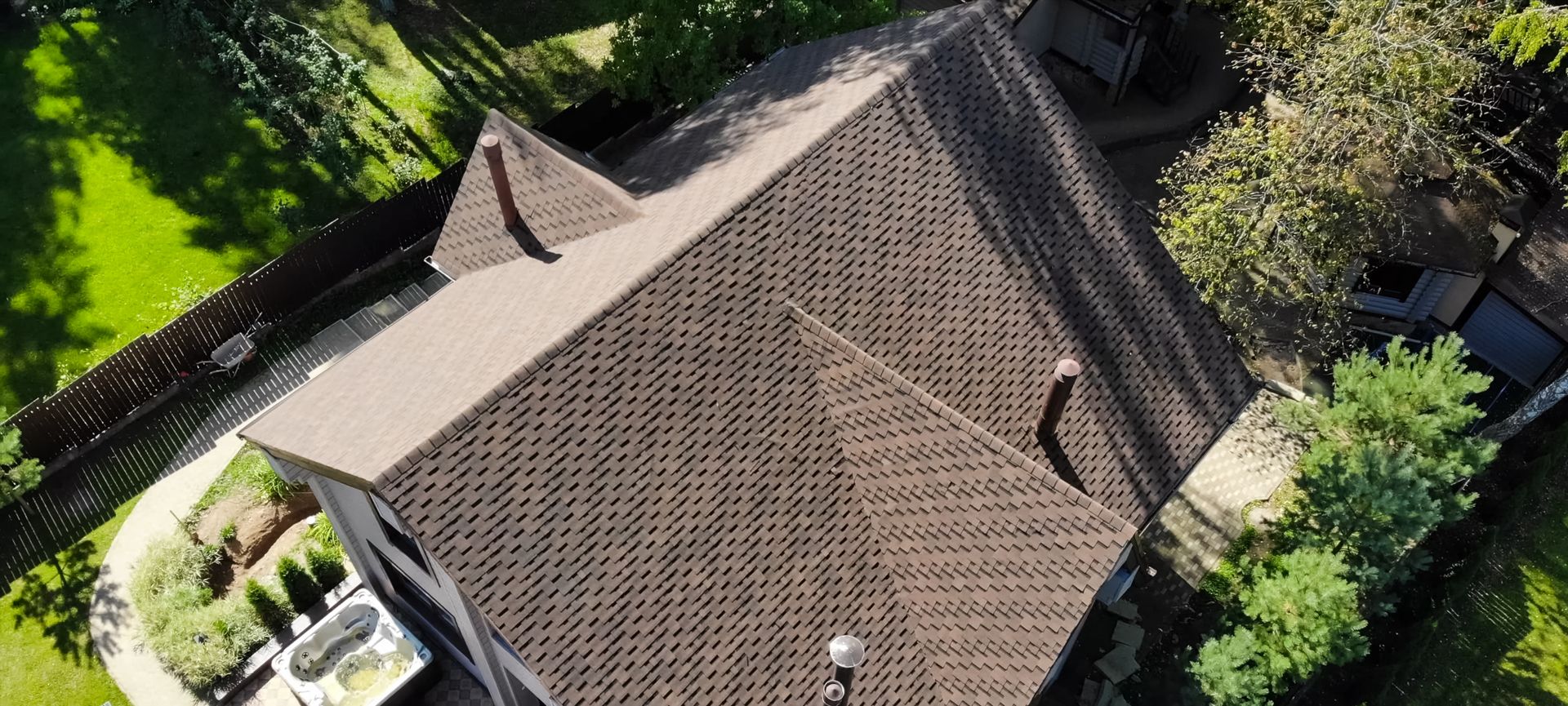 Aerial view of a brown tile roof with chimneys. Green trees and lawn surround the house.