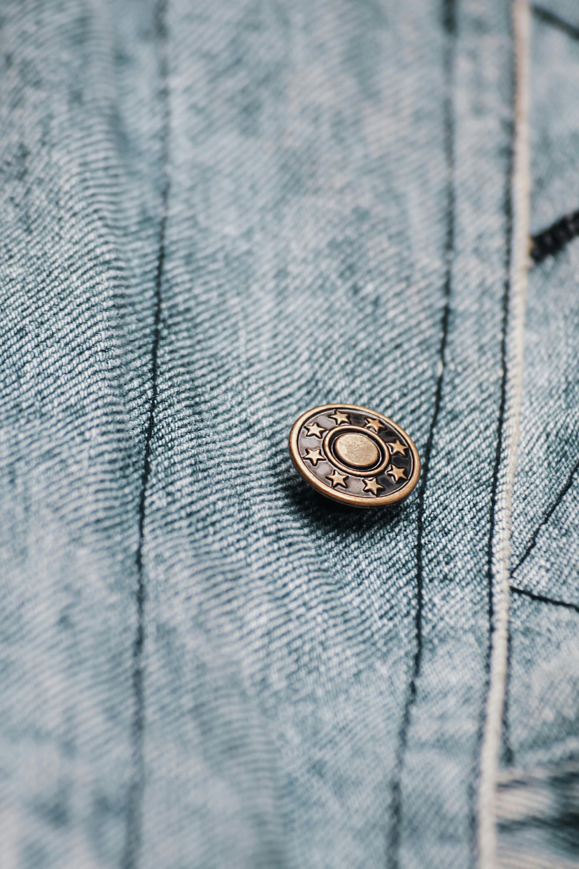 Close-up of a decorative button on light blue denim fabric.