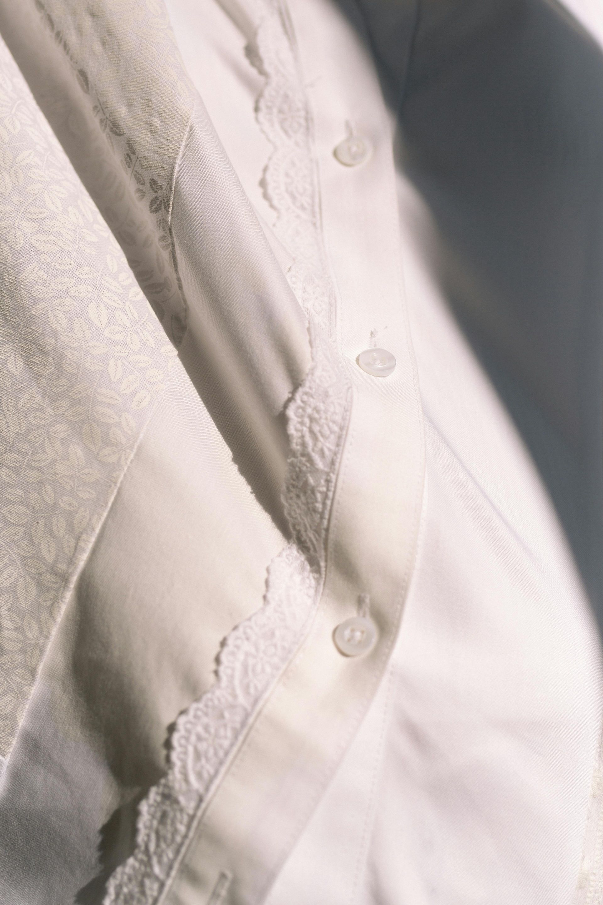 Close-up of a white button-up shirt with frayed seams and torn fabric along the front edge