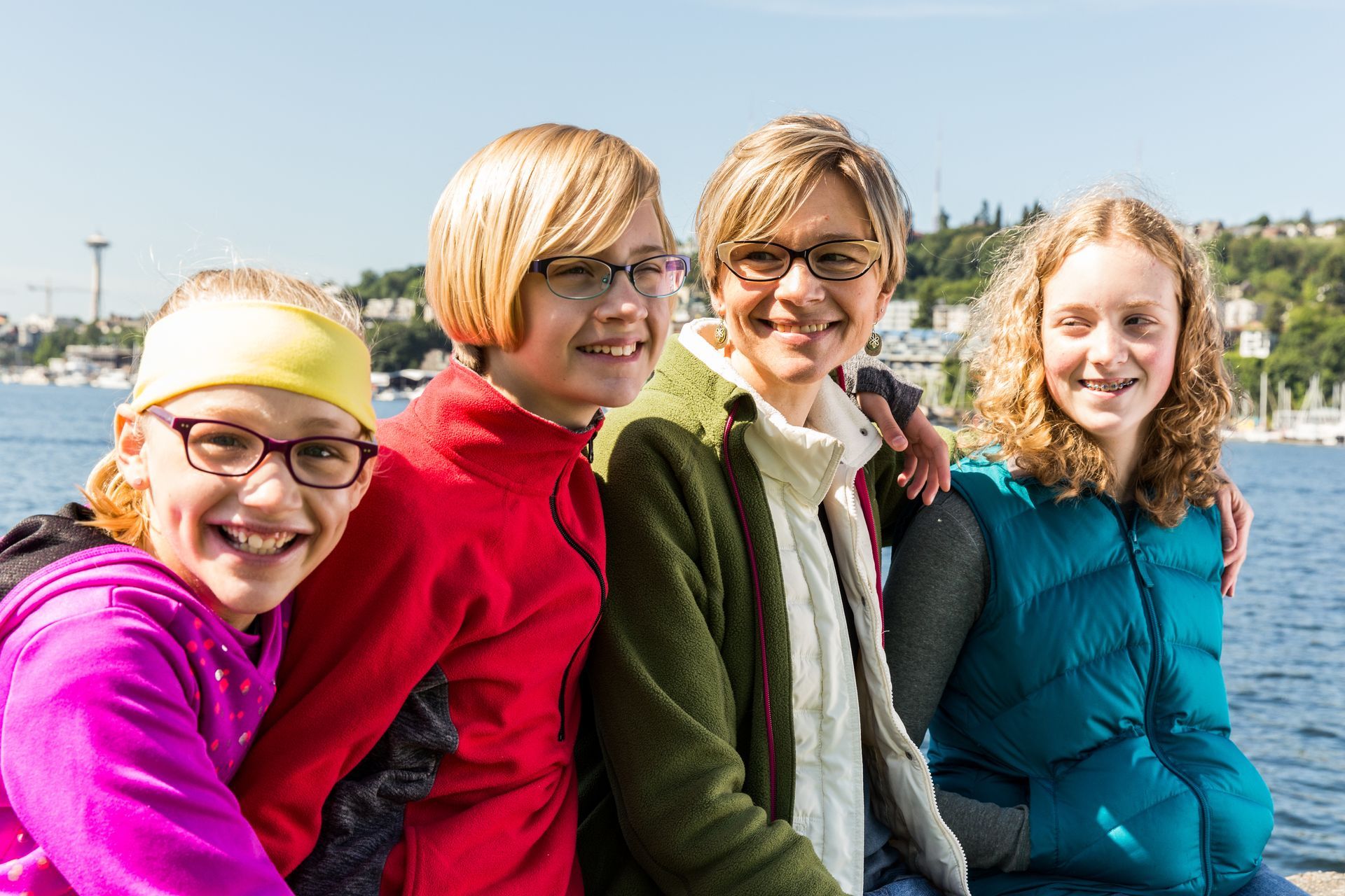 Four people smiling, posing outdoors by water; Seattle skyline in the background.