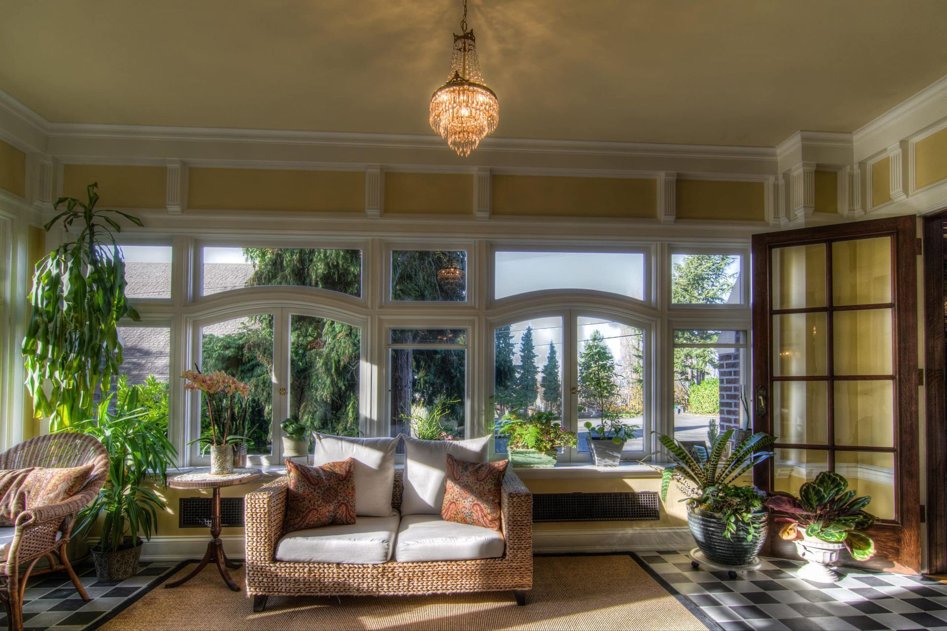 A living room with a couch , chairs , plants and a chandelier.