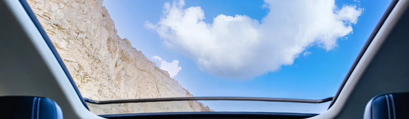 Vista dall'interno di un'auto attraverso il tettuccio apribile di scogliere rocciose e cielo azzurro con nuvole.
