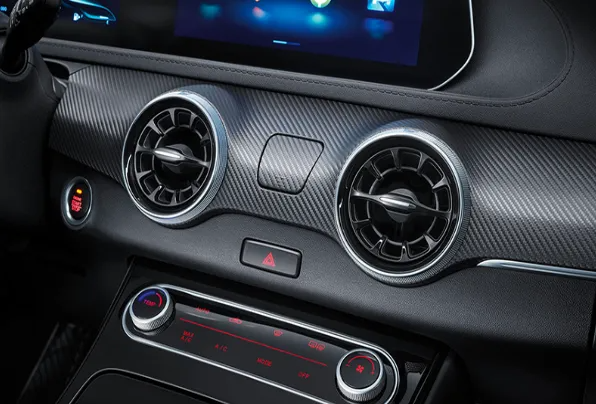 Console del cruscotto dell'auto con due bocchette d'aria, pulsante delle luci di emergenza e comandi del climatizzatore.