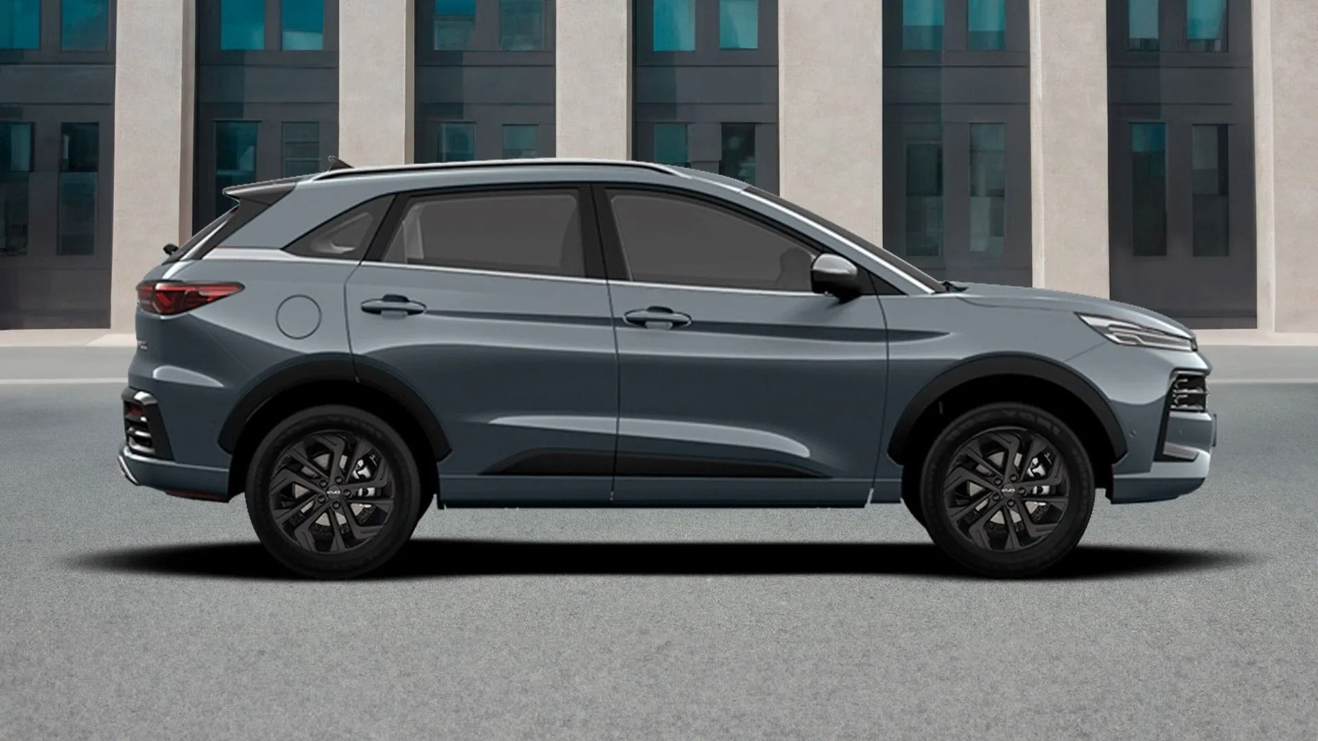 Un SUV grigio è parcheggiato di profilo su una strada cittadina, di fronte a un edificio moderno.