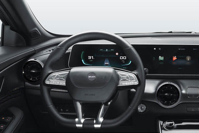 Cruscotto interno dell'auto con volante, display digitali e console centrale con finiture scure.