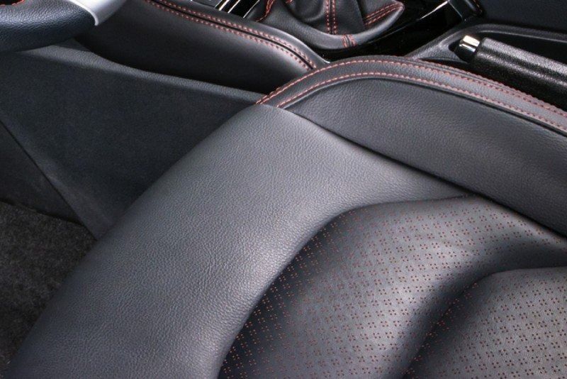 Primo piano di sedili per auto in pelle nera con cuciture rosse e rivestimento traforato.