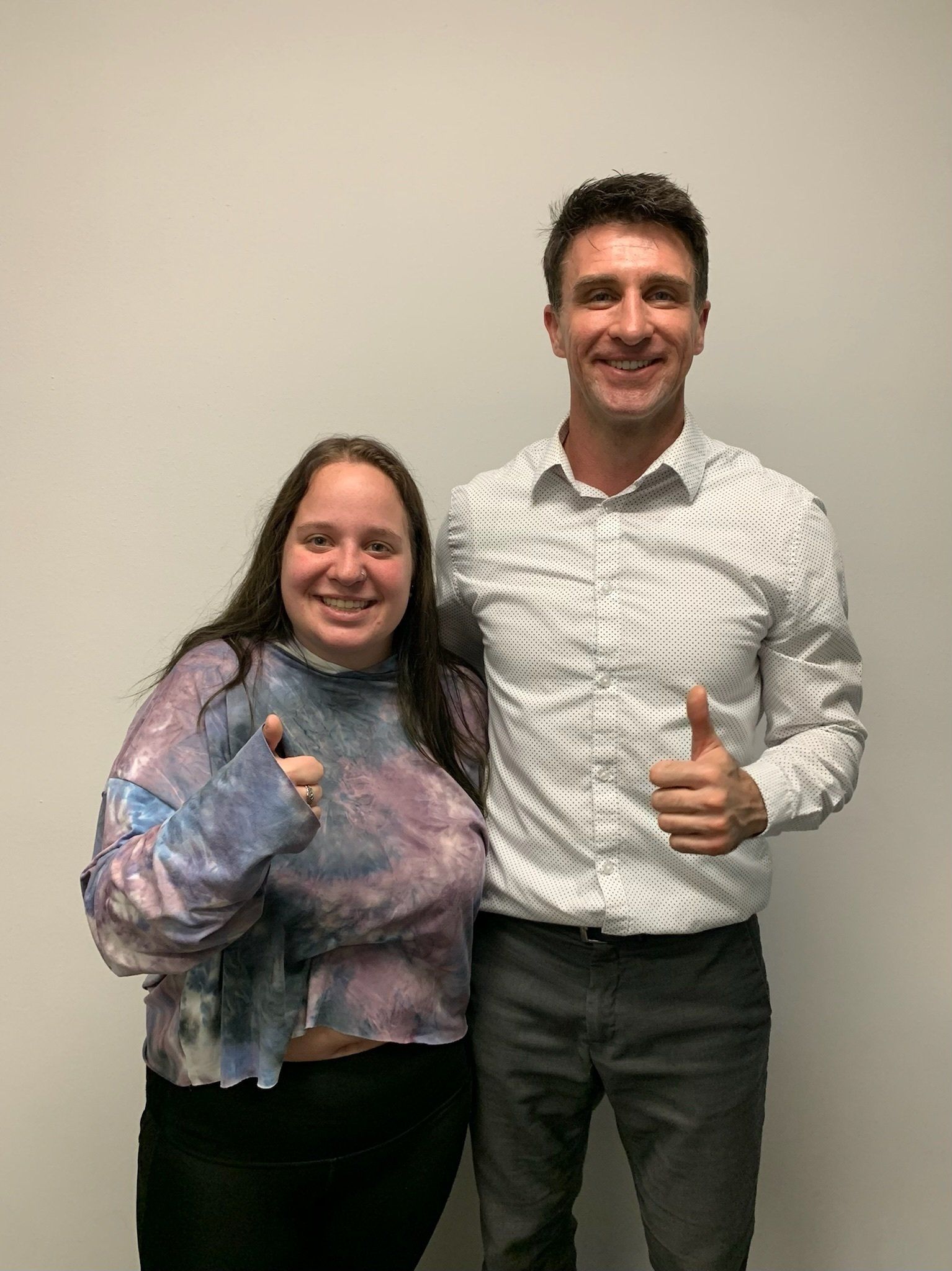 A man and a woman are standing next to each other and giving a thumbs up.