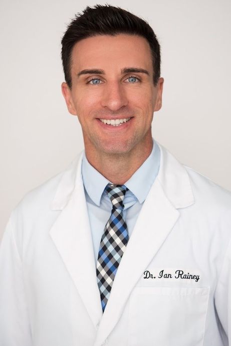 A man in a lab coat and tie is smiling for the camera.