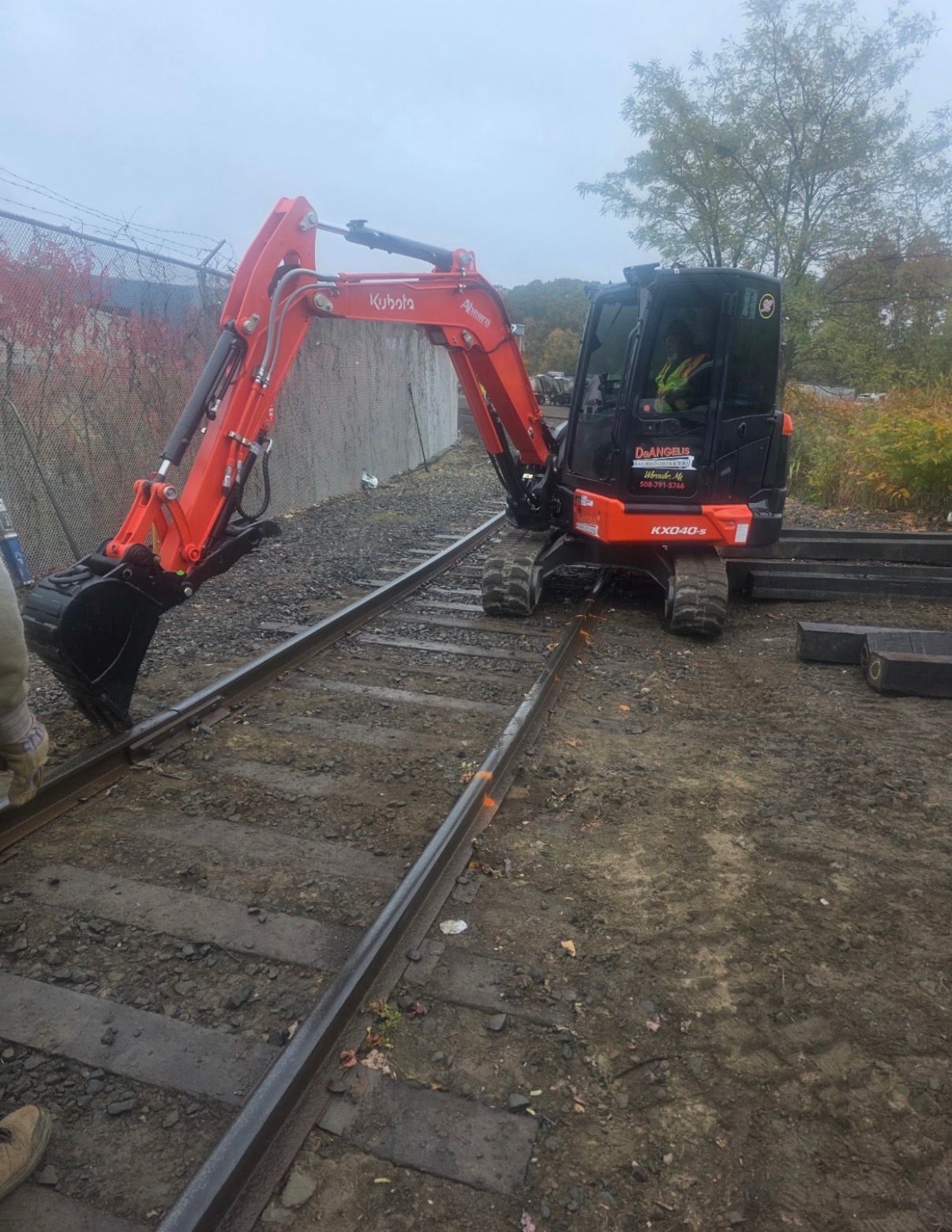 Orange excavator working beside railway tracks near a black truck in a muddy outdoor yard.