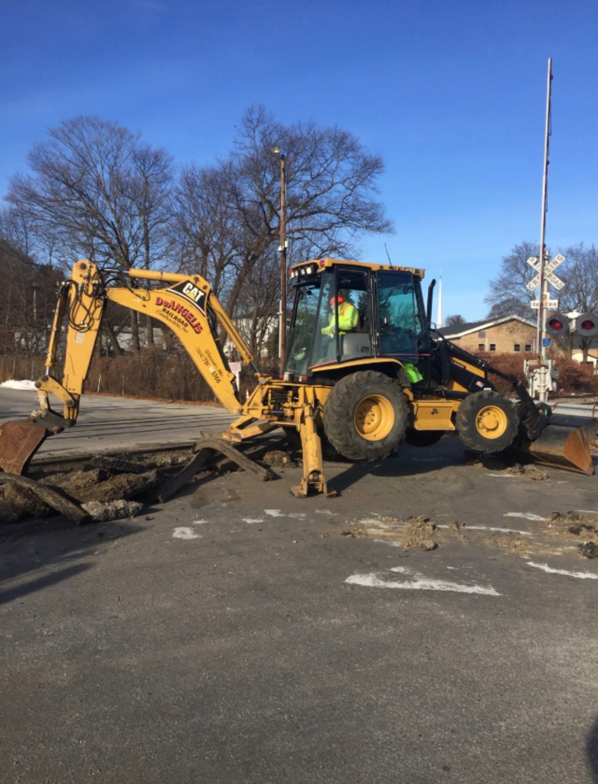 Yellow backhoe excavator digging up road at a construction site on a sunny day