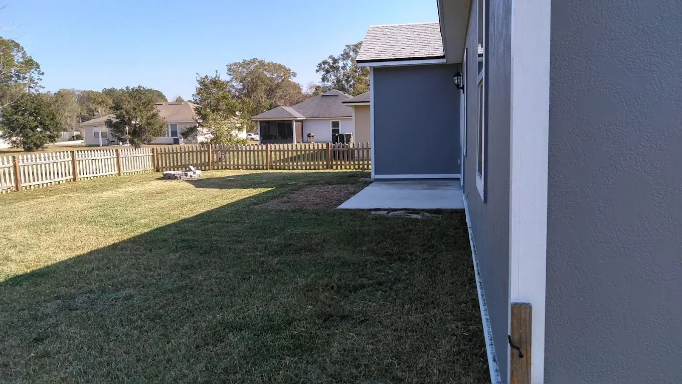 A backyard with a fence and a house in the background.