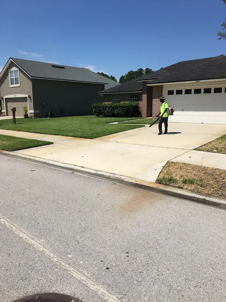 A man is blowing grass in front of a house.