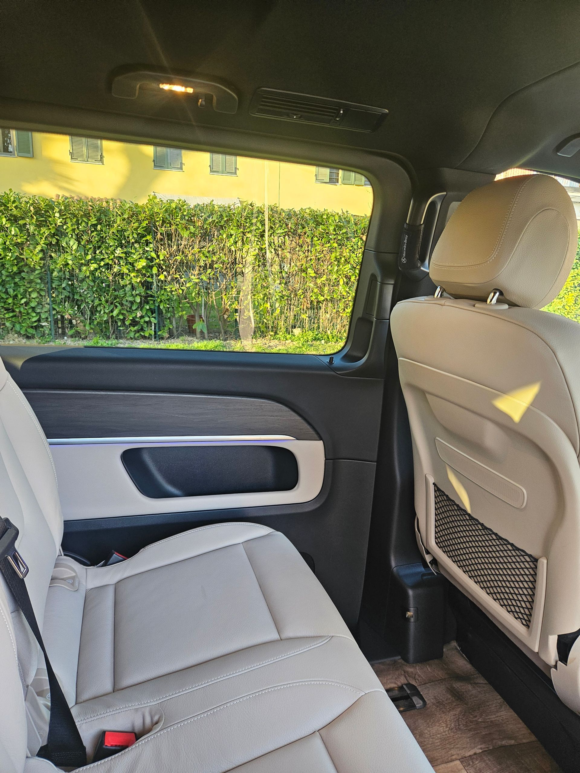 Interno di un furgone Mercedes beige, con sedili posteriori, finestrini e pannelli delle portiere con illuminazione ambientale.