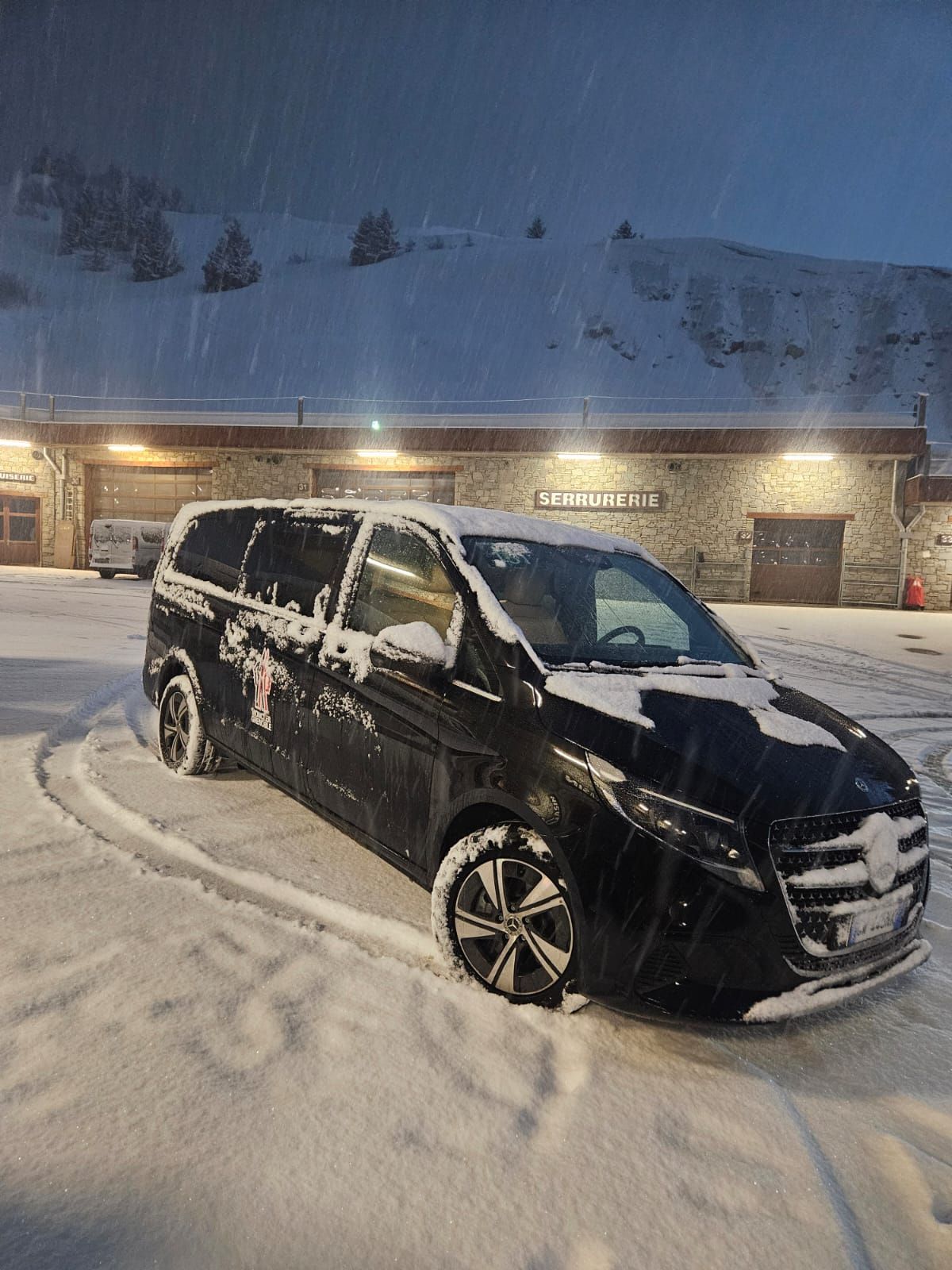 Furgone nero coperto di neve parcheggiato di fronte a un edificio in un resort di montagna innevato.