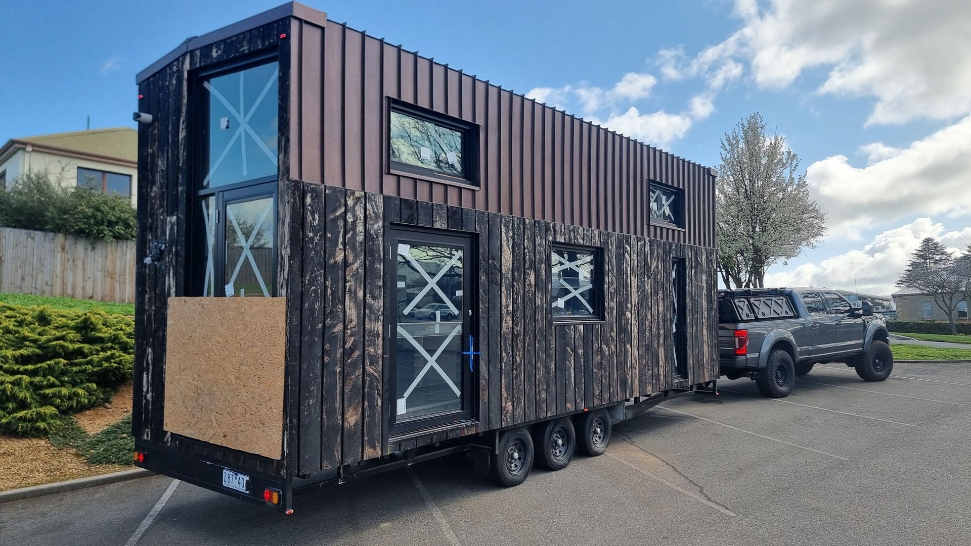A tiny house is being towed by a truck in a parking lot.