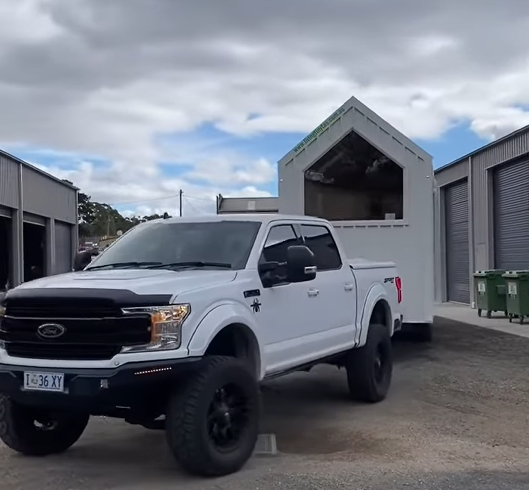 A white truck with a trailer attached to it is parked in a parking lot.