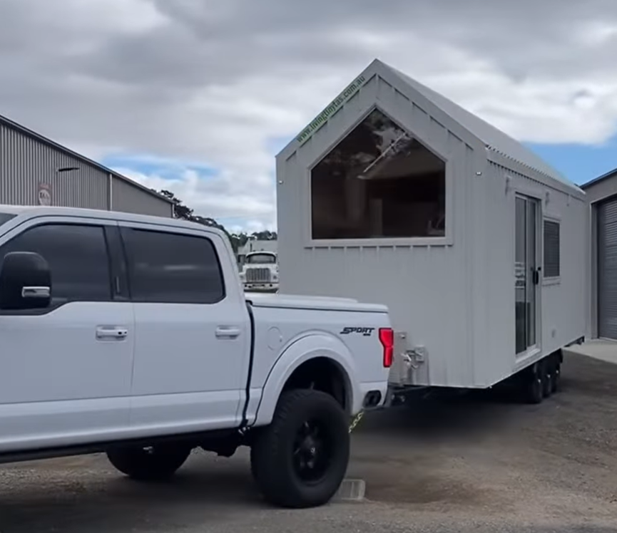 A white truck is pulling a trailer that looks like a house.
