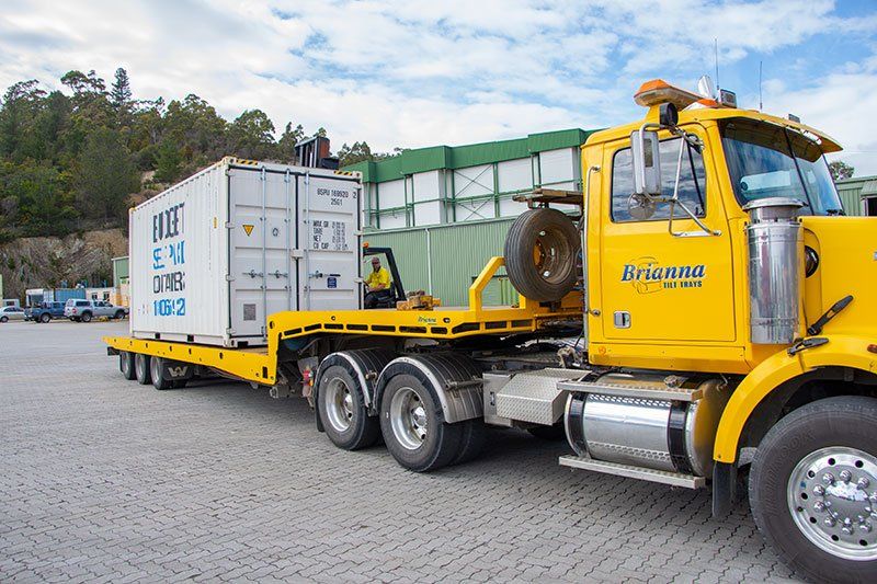Brianna's flatbed tow truck hauling a metal container.