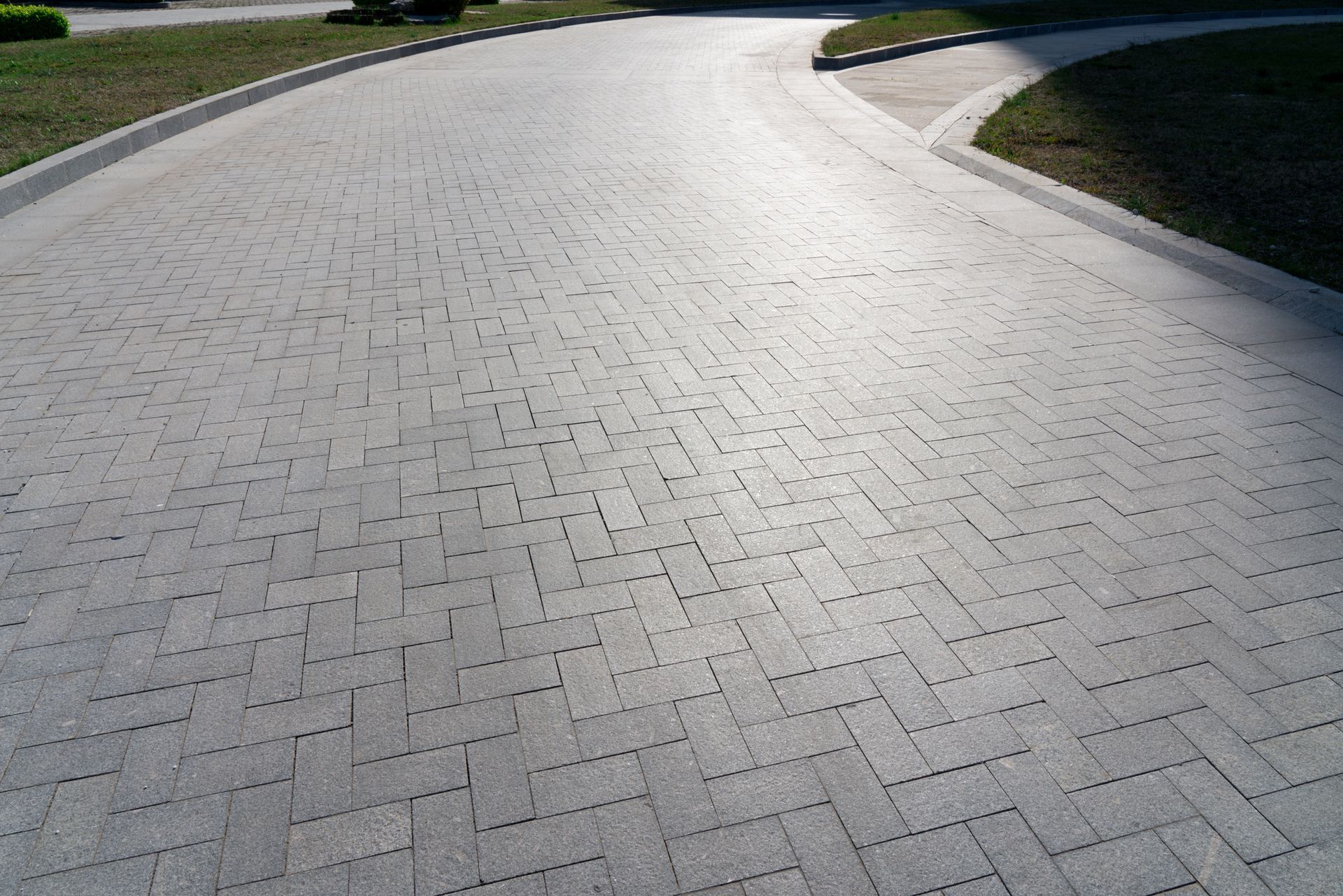 Curved paved pathway with interlocking bricks and grass on both sides.