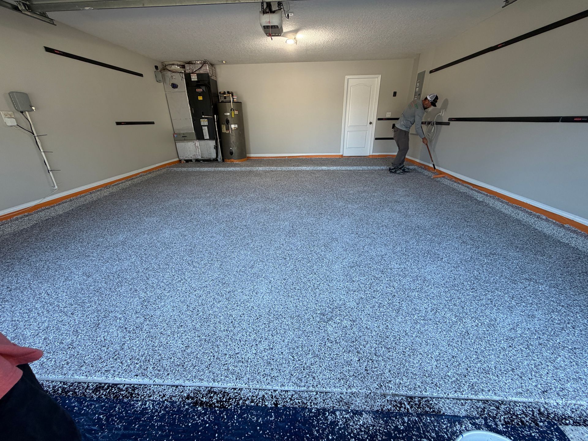 Garage with speckled epoxy floor, white walls, and a person working on the floor.