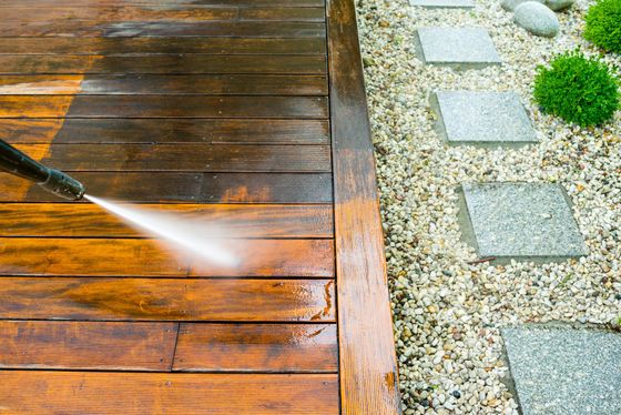 Pressure washing wood deck to remove dirt and restore natural color beside gravel garden.