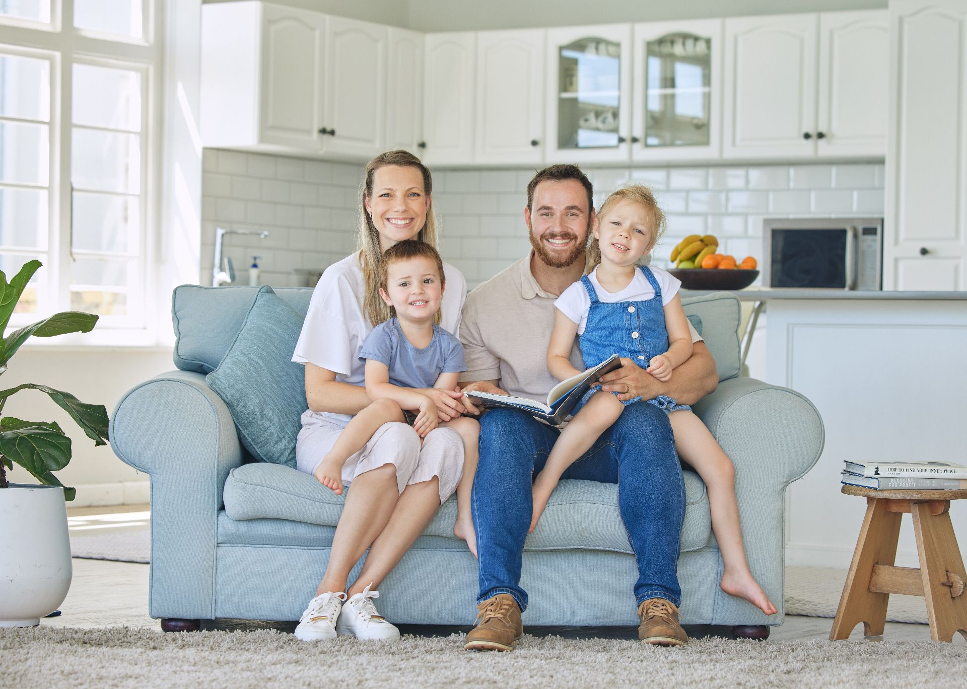Family sitting on a light blue couch in a bright living room, smiling at the camera.