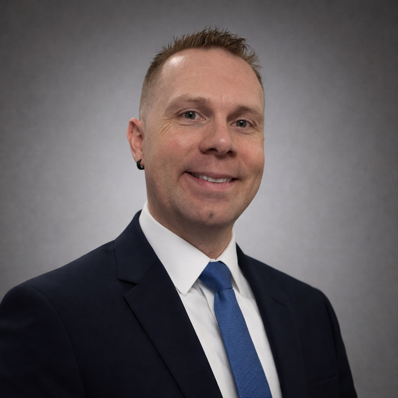 Professional headshot of a smiling person in a dark suit, blue tie, and white shirt against a gray background
