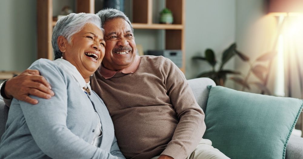 Smiling couple on a couch looking at a smartphone in a bright living room