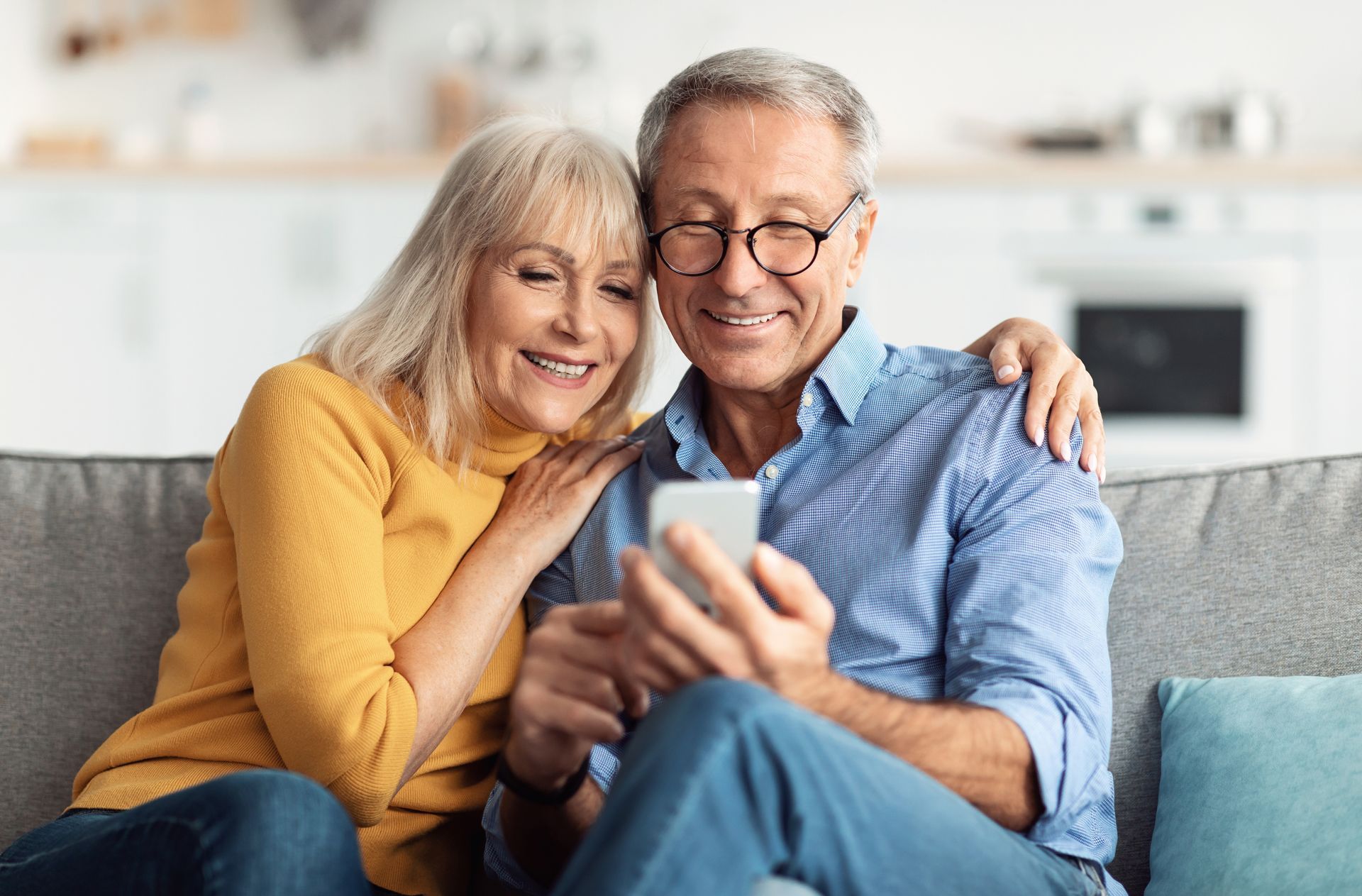 Smiling couple on a couch looking at a smartphone in a bright living room