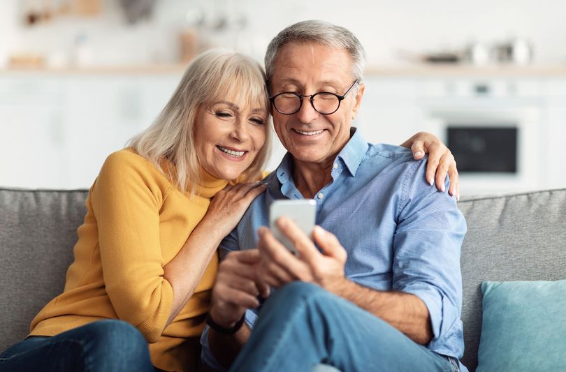Smiling couple on a couch looking at a smartphone in a bright living room