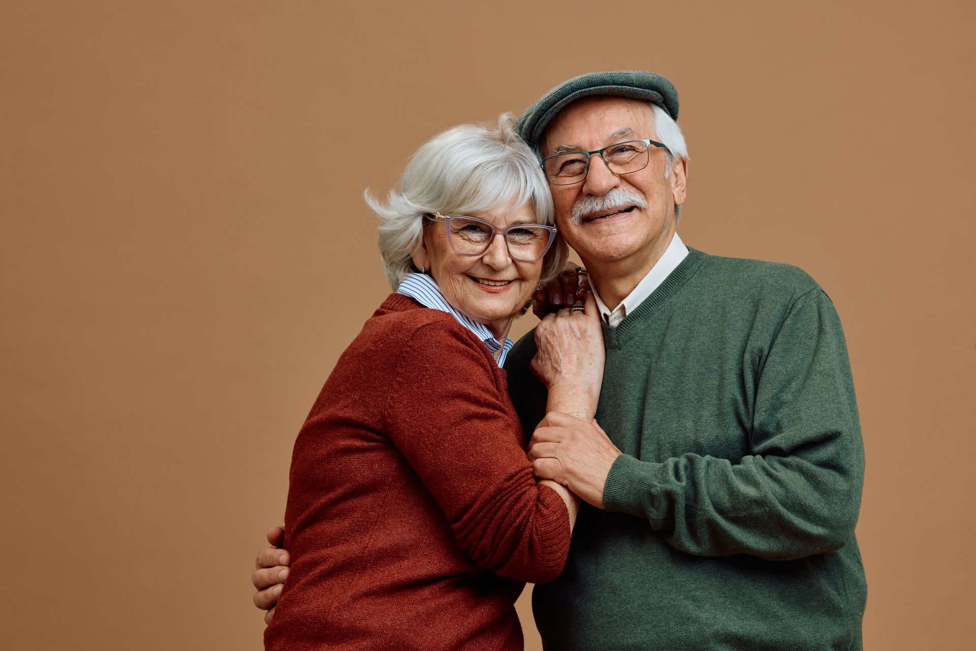 Two smiling people in sweaters and hats posing closely against a plain brown background