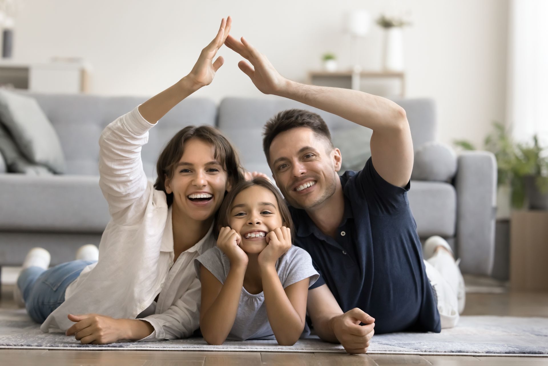 Family of three smiling and lying on the floor with hands joined in a triangle in a bright living room