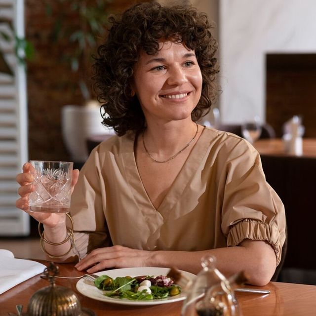 A woman is sitting at a table with a plate of food and a glass of wine.