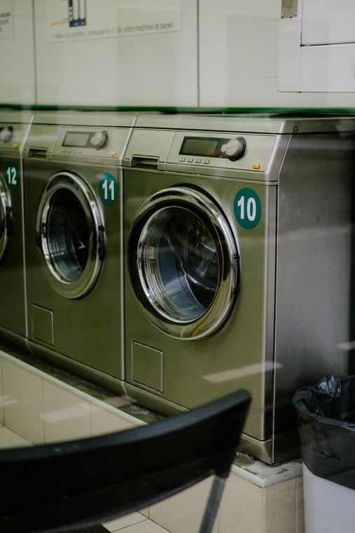 A row of industrial stainless steel washing machines, numbered 10, 11, and 12, in a brightly lit laundromat.