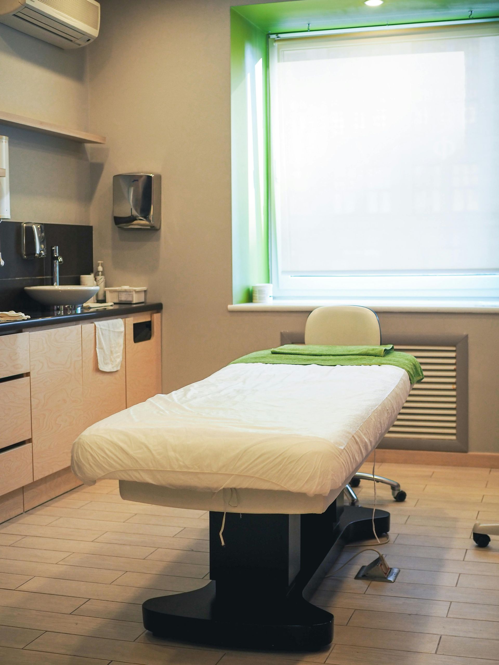 Treatment room with an exam table, cabinets, sink, and a large bright window
