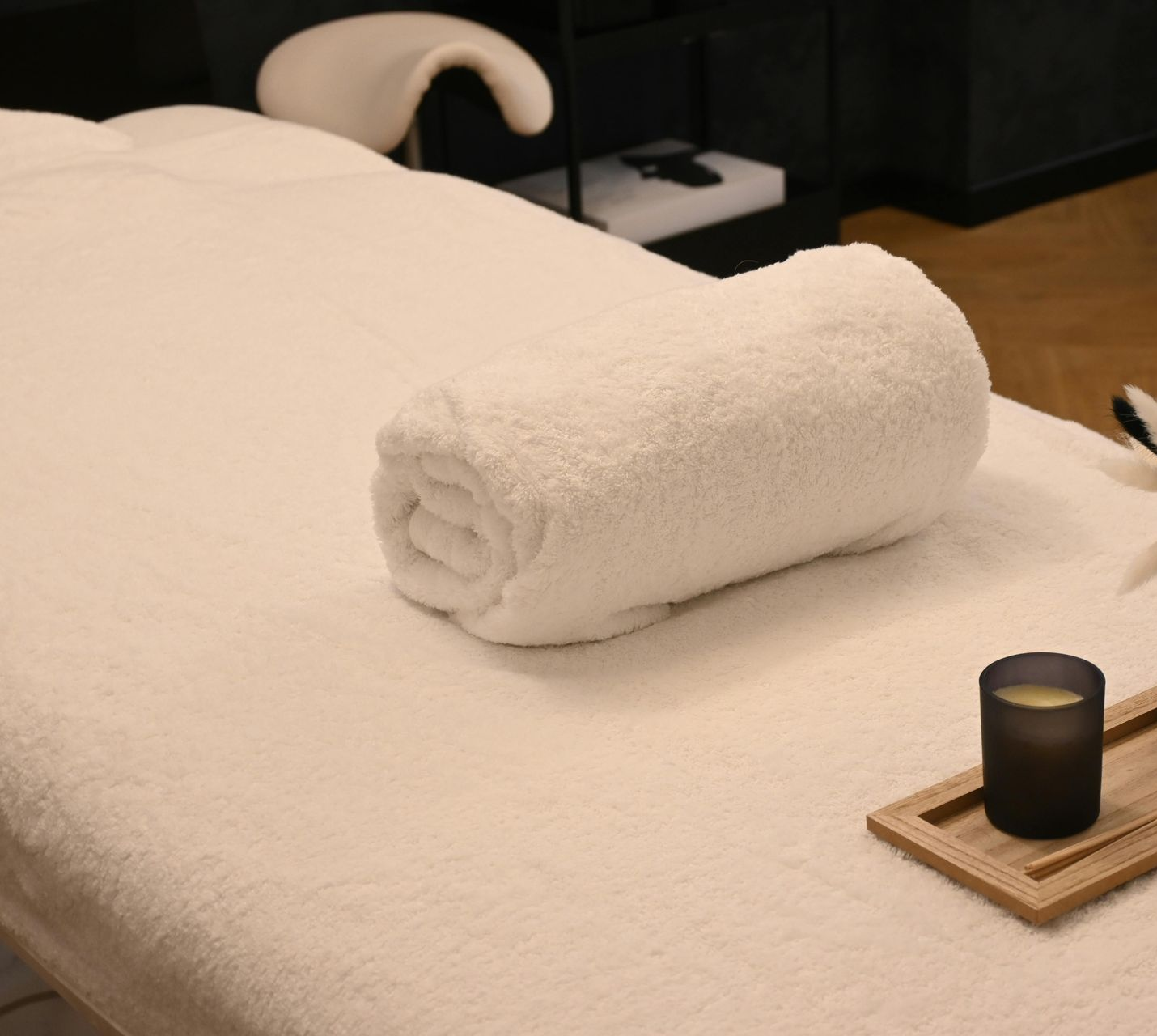 Tidy bedroom with a cream bedspread, rolled towel, and bedside tray with candle and reeds