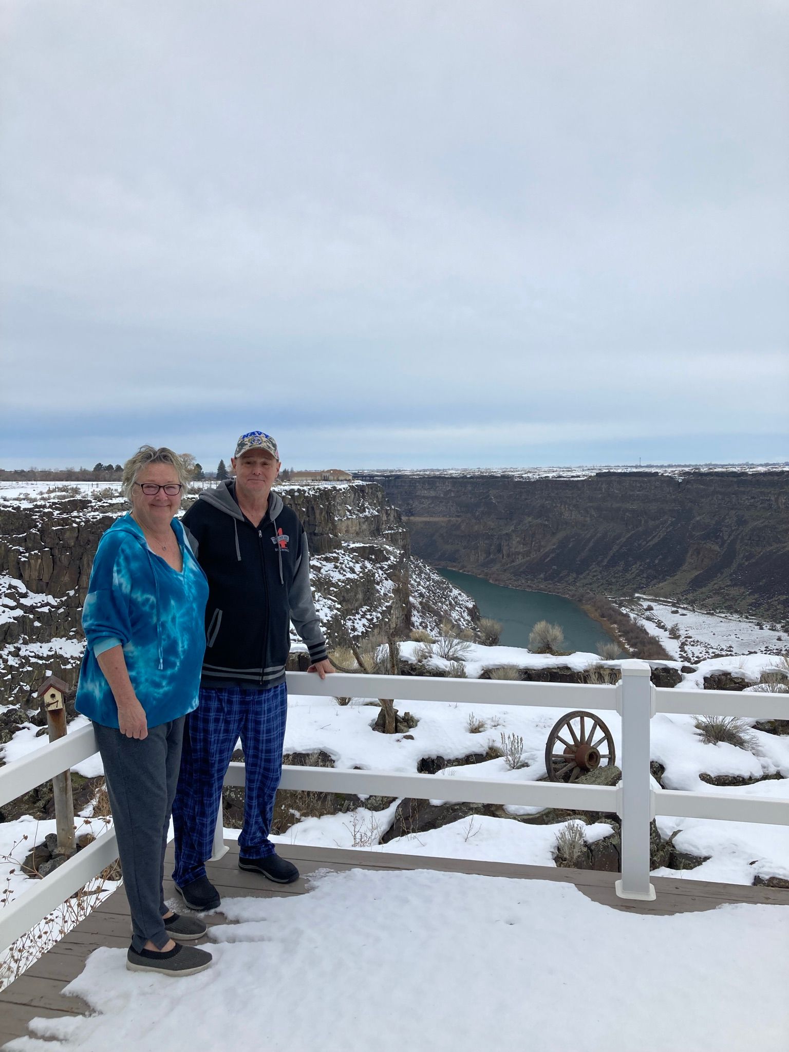A man and a woman are standing on a snowy ledge overlooking a river.