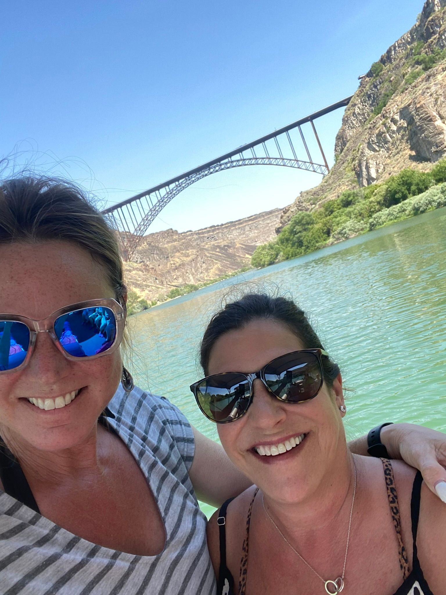 Two women wearing sunglasses are posing for a picture next to a body of water.