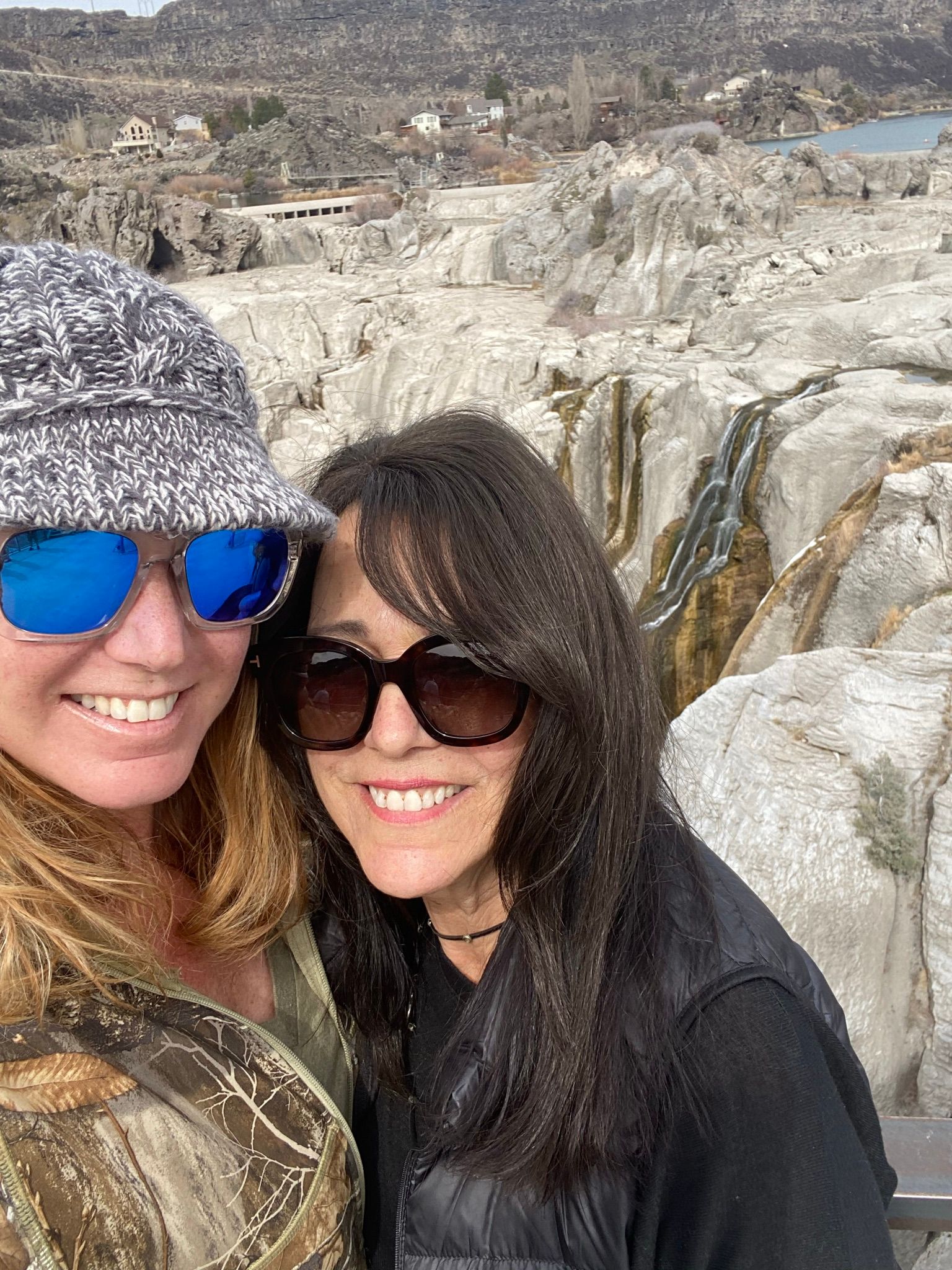 Two women wearing sunglasses and a hat are posing for a picture.