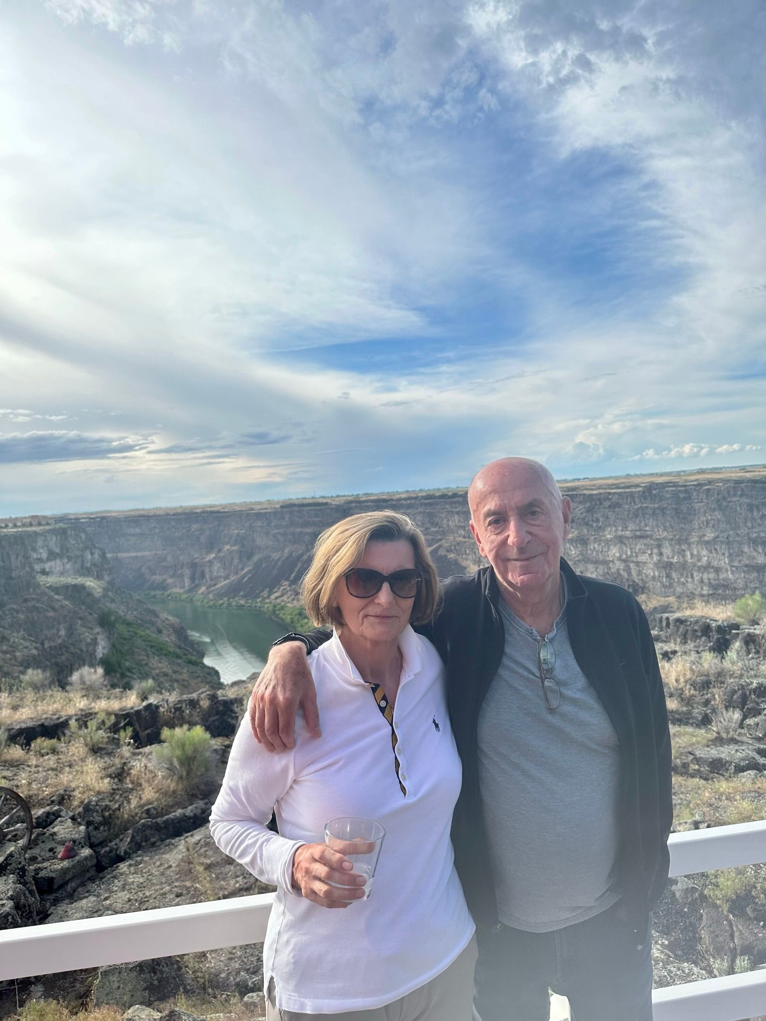 A man and a woman are standing next to each other on a balcony overlooking a river.