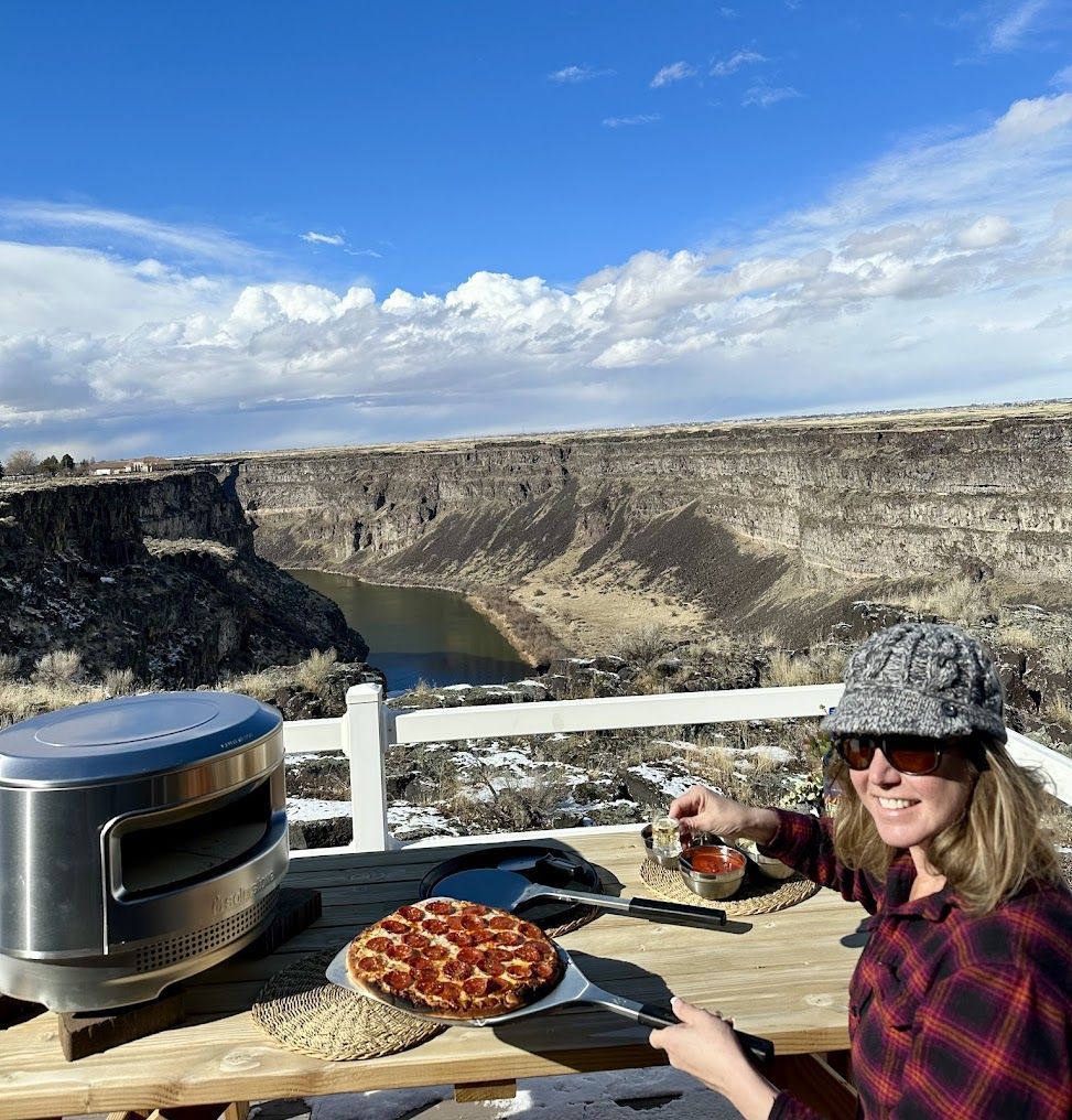 A woman is sitting at a table with a pizza in front of a canyon.