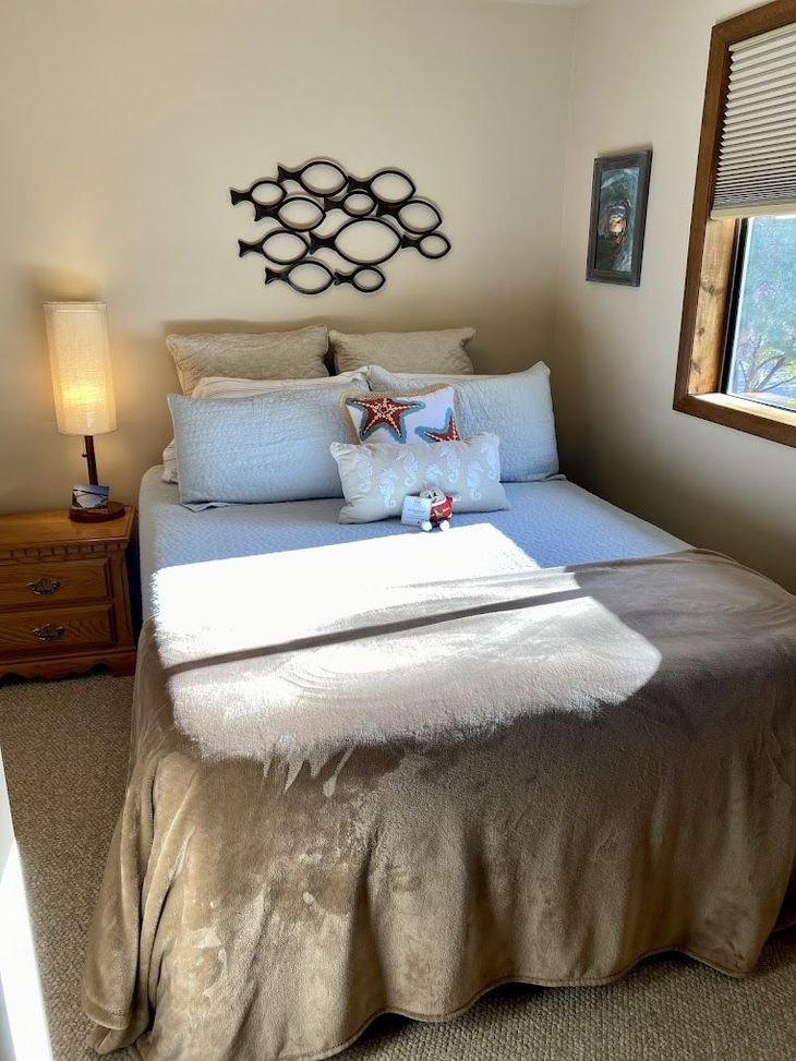 Cozy bedroom with made bed, lamp on nightstand, wall art, and window light