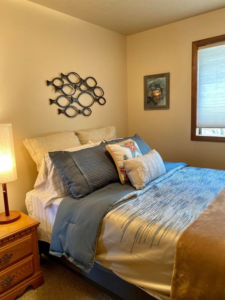 Cozy bedroom with a neatly made bed, bedside lamp, wall art, and a window with blinds.