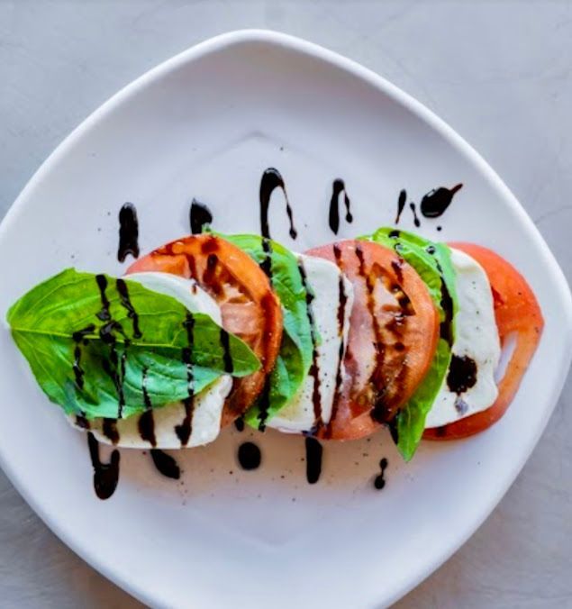 A white plate topped with sliced tomatoes cheese and basil