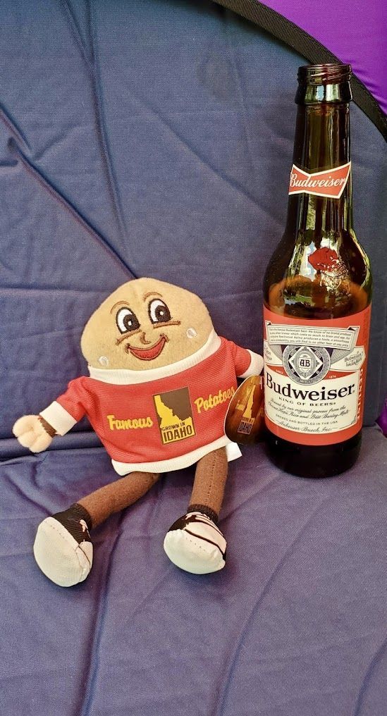 A stuffed egg is sitting next to a bottle of budweiser beer.