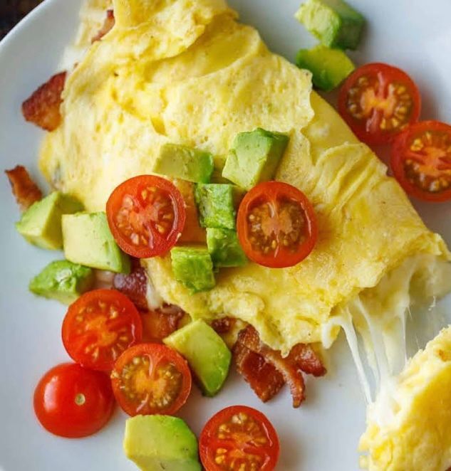 An omelet with tomatoes , avocado , bacon and cheese on a white plate.