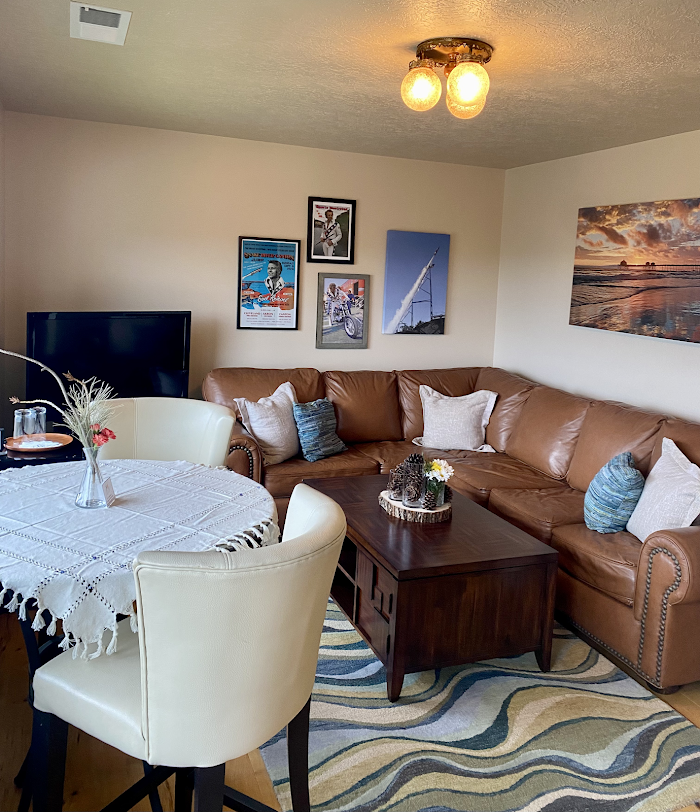 Cozy living room with tan sectional, round dining table, TV, wall art, and wavy-pattern rug