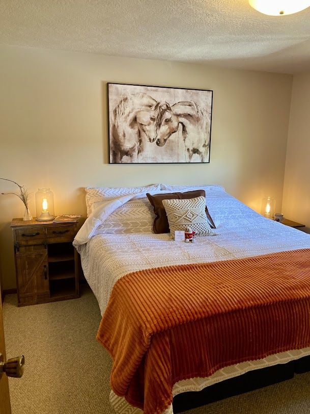 Cozy bedroom with a made bed, orange throw, bedside table, and cow painting above the headboard