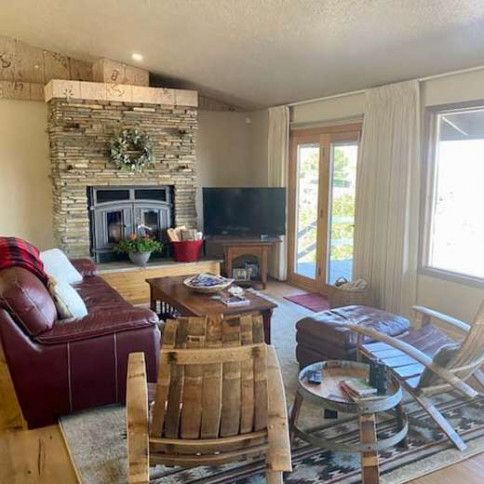 Cozy living room with brick fireplace, red sofa, TV, wooden chairs, and bright French doors