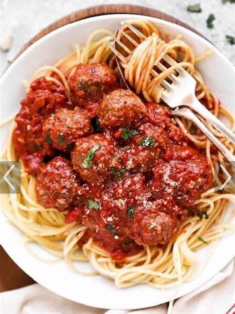 Spaghetti with meatballs and rich red tomato sauce in a white bowl, fork in the pasta.